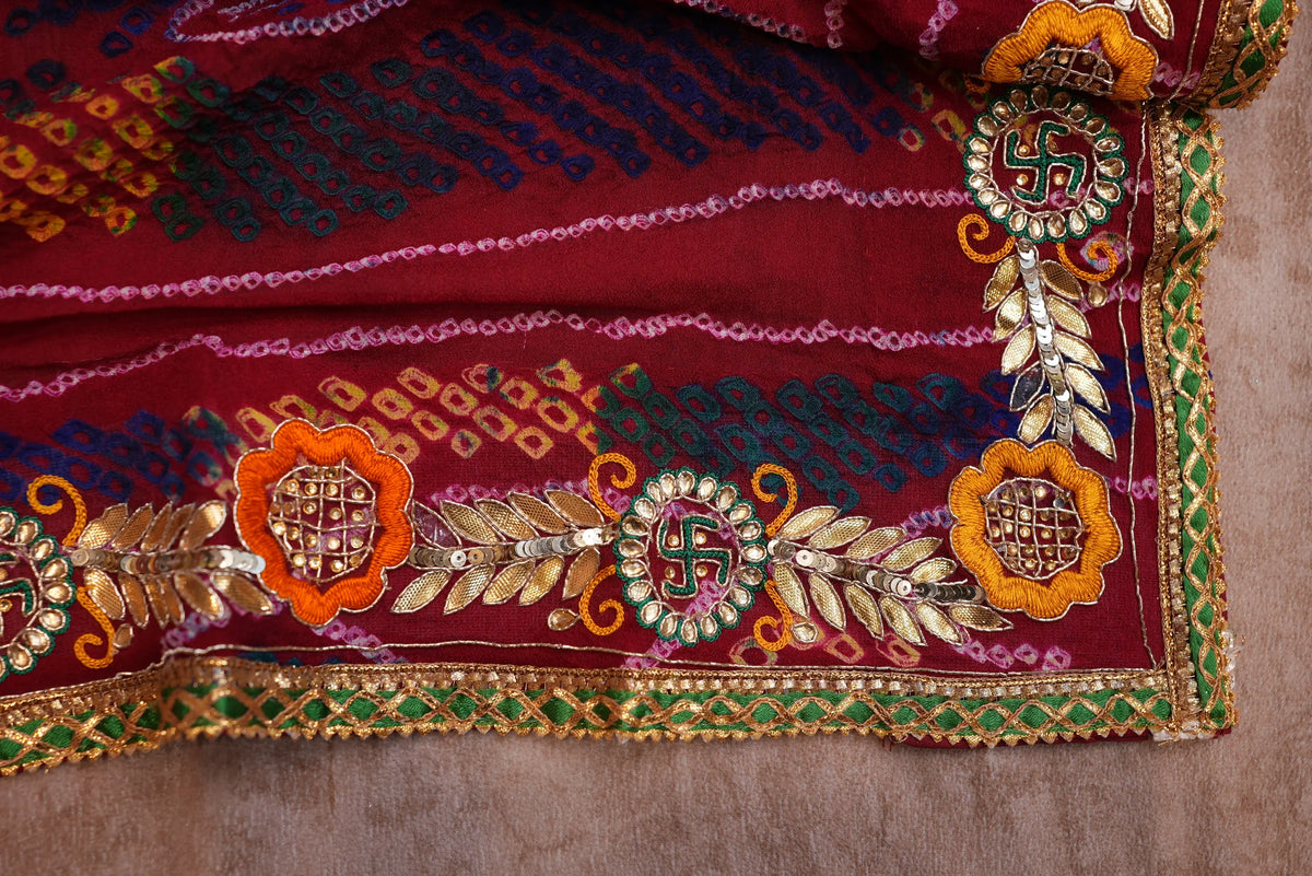 Extreme close-up of Swastik motif, yellow floral applique, leaf sequin work, and green lace border
