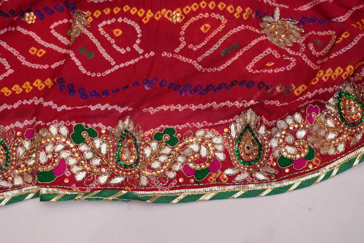 Close-up shot of heavy Kundan, Cut Dana, and emerald green Meenakari border work on red Bandhani Dupatta
