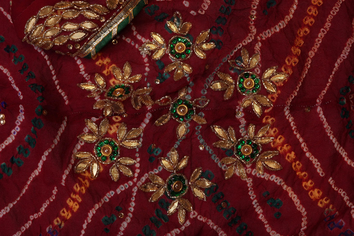 Macro close-up of gold Zardozi flower motifs with vibrant emerald-green centers on red Ojariya Bandhej fabric