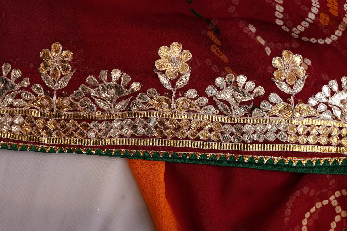 Macro close-up of intricate Kaccha Gota Patti floral border with sequin accents on red georgette fabric