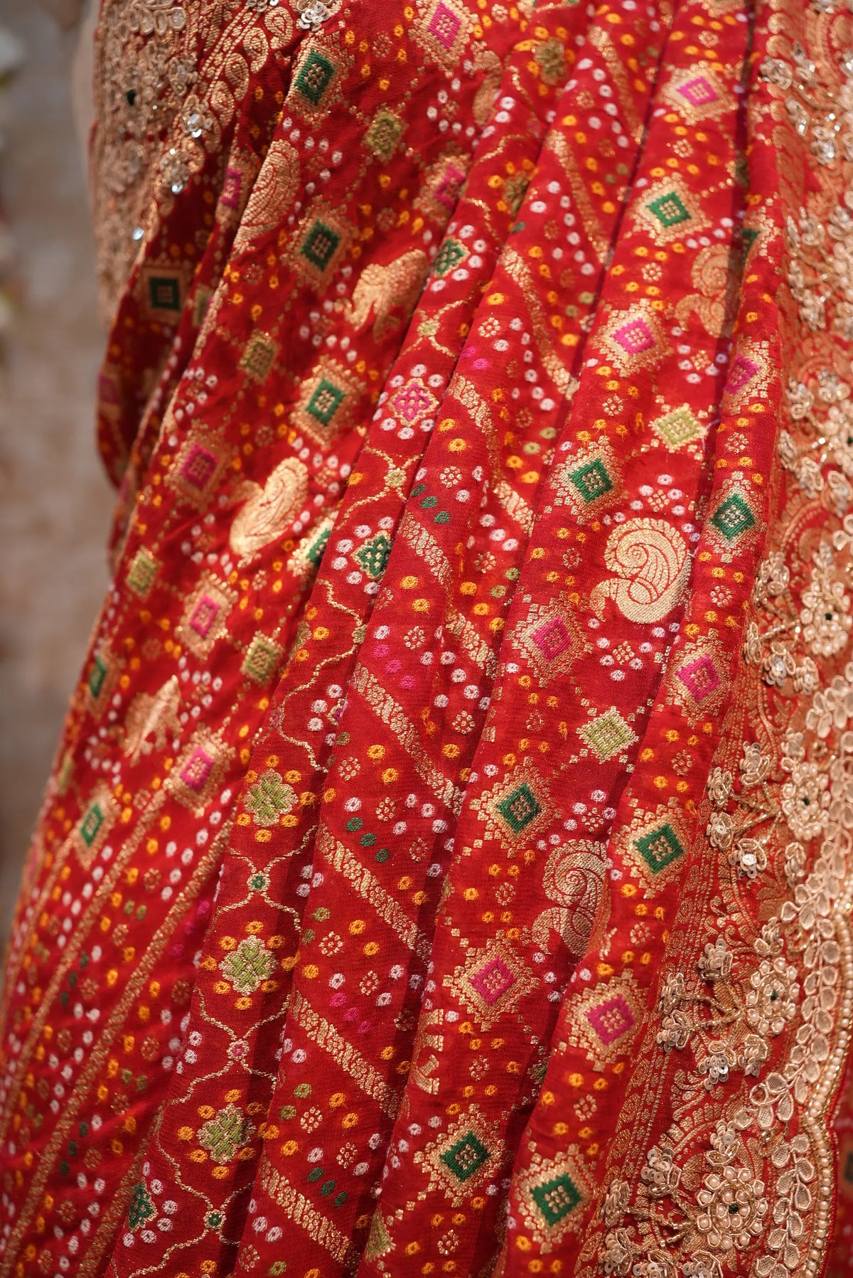 Close-up macro shot of woven bandhani print and zari motifs on pure red georgette fabric