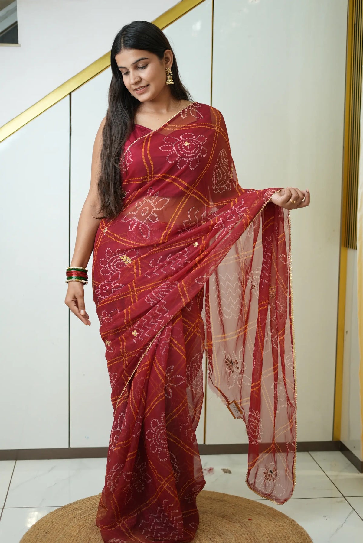 Model draped in maroon chiffon bandhani saree featuring gota patti buttas and golden lace border