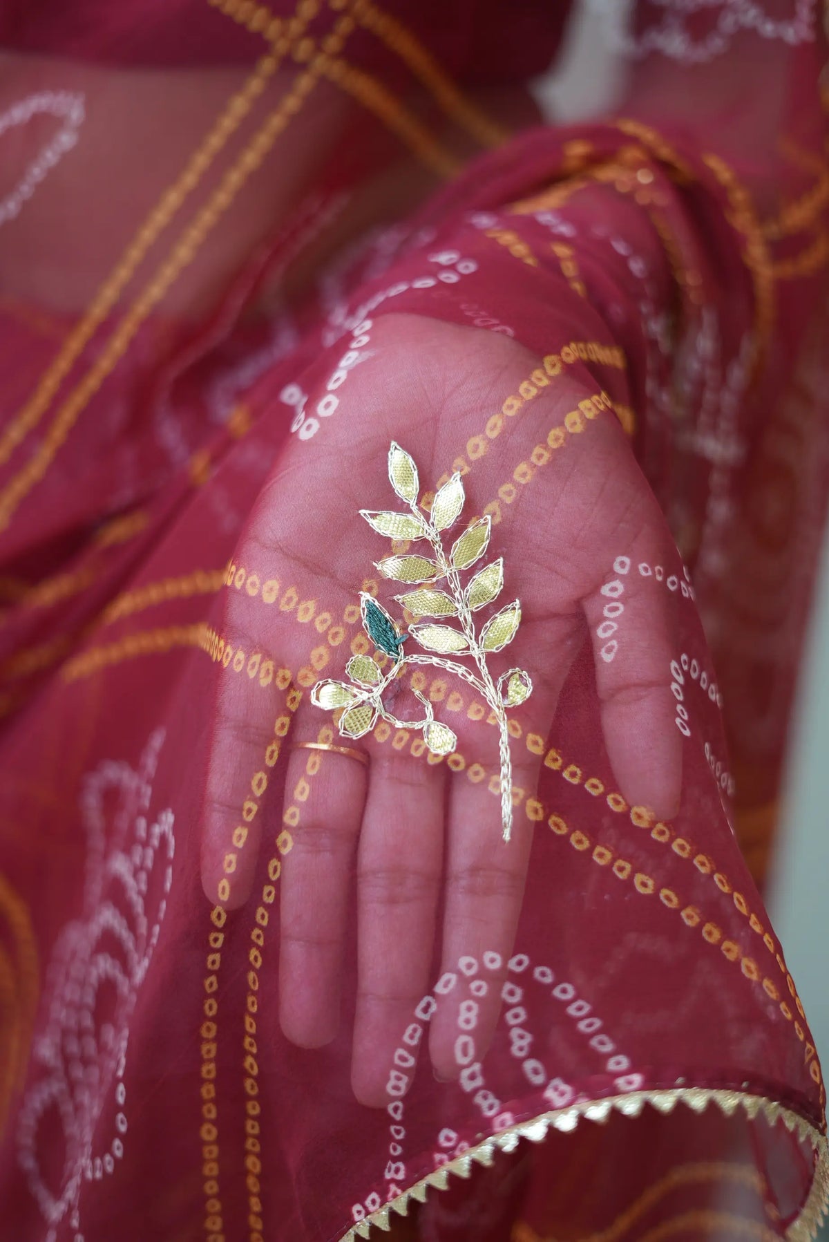 Macro view of handcrafted gold leaf and branch gota patti work on maroon bandhej saree