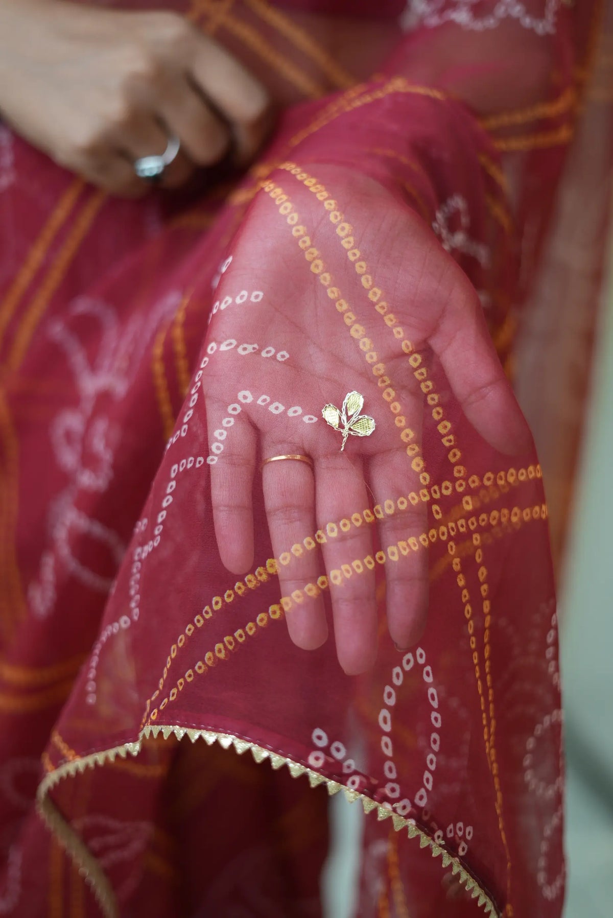 Close-up shot of golden leaf-shaped gota patti motif on maroon chiffon bandhani fabric