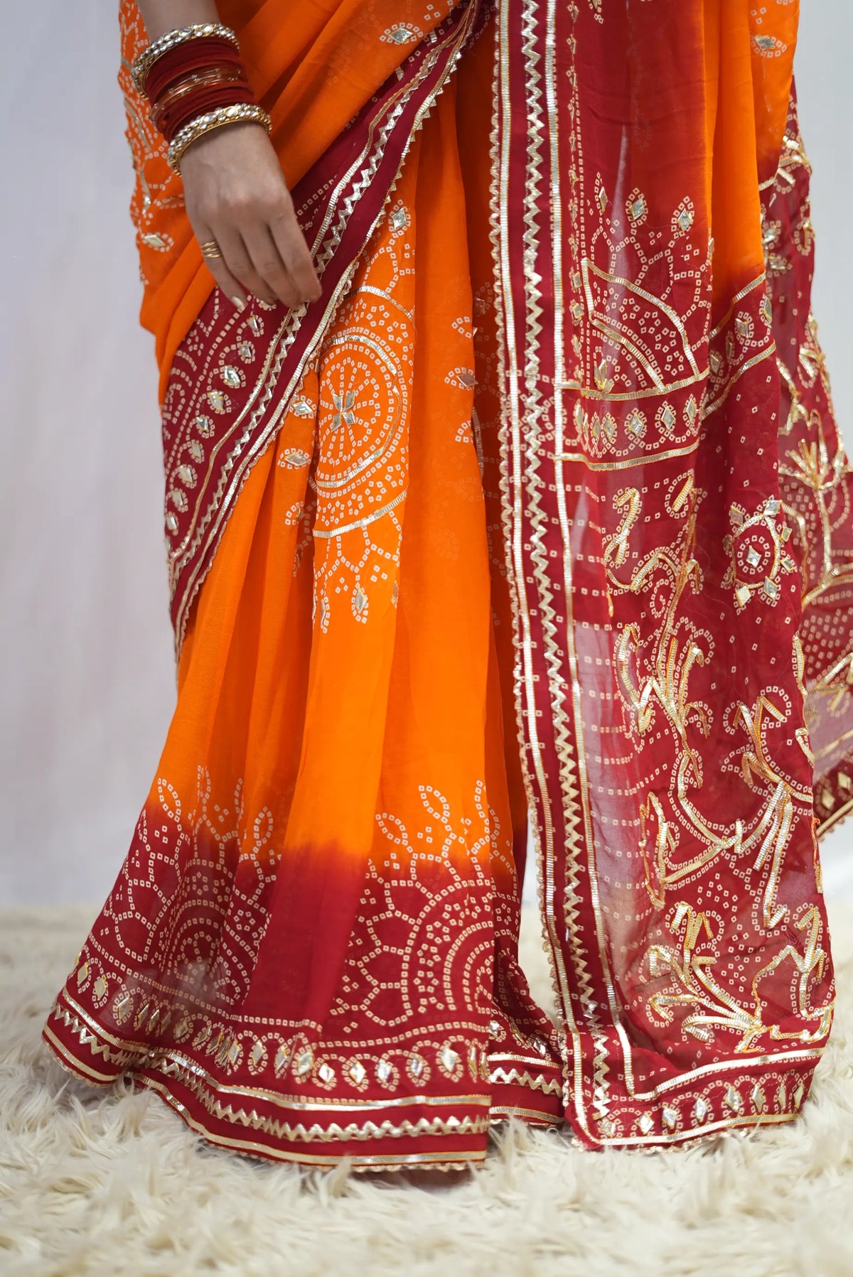 Lower pleats and border detail of yellow and red georgette bandhani saree with gota patti work