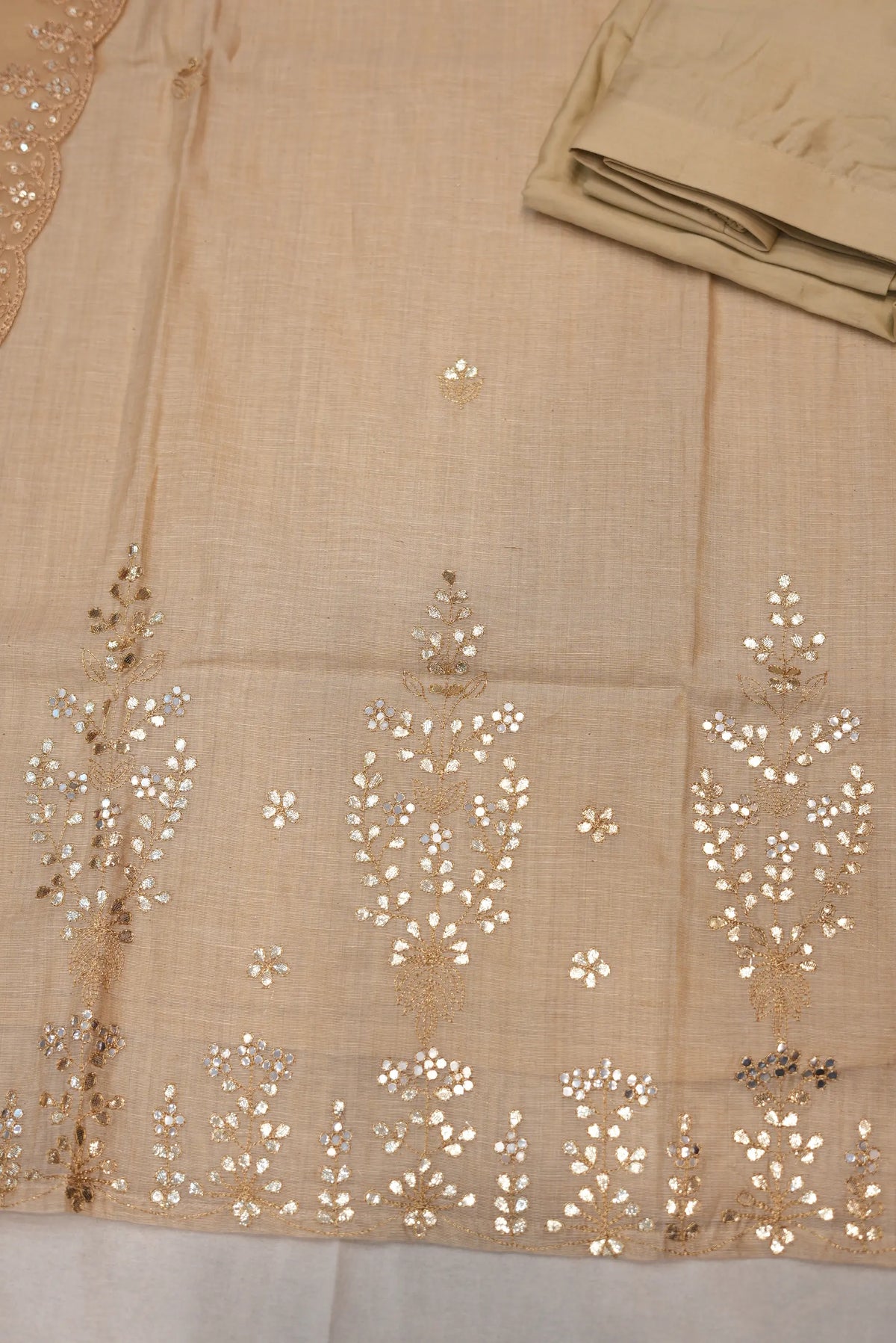 Detailed view of lower hemline on beige cotton khadi kurta showing leaf pattern gotta patti embroidery