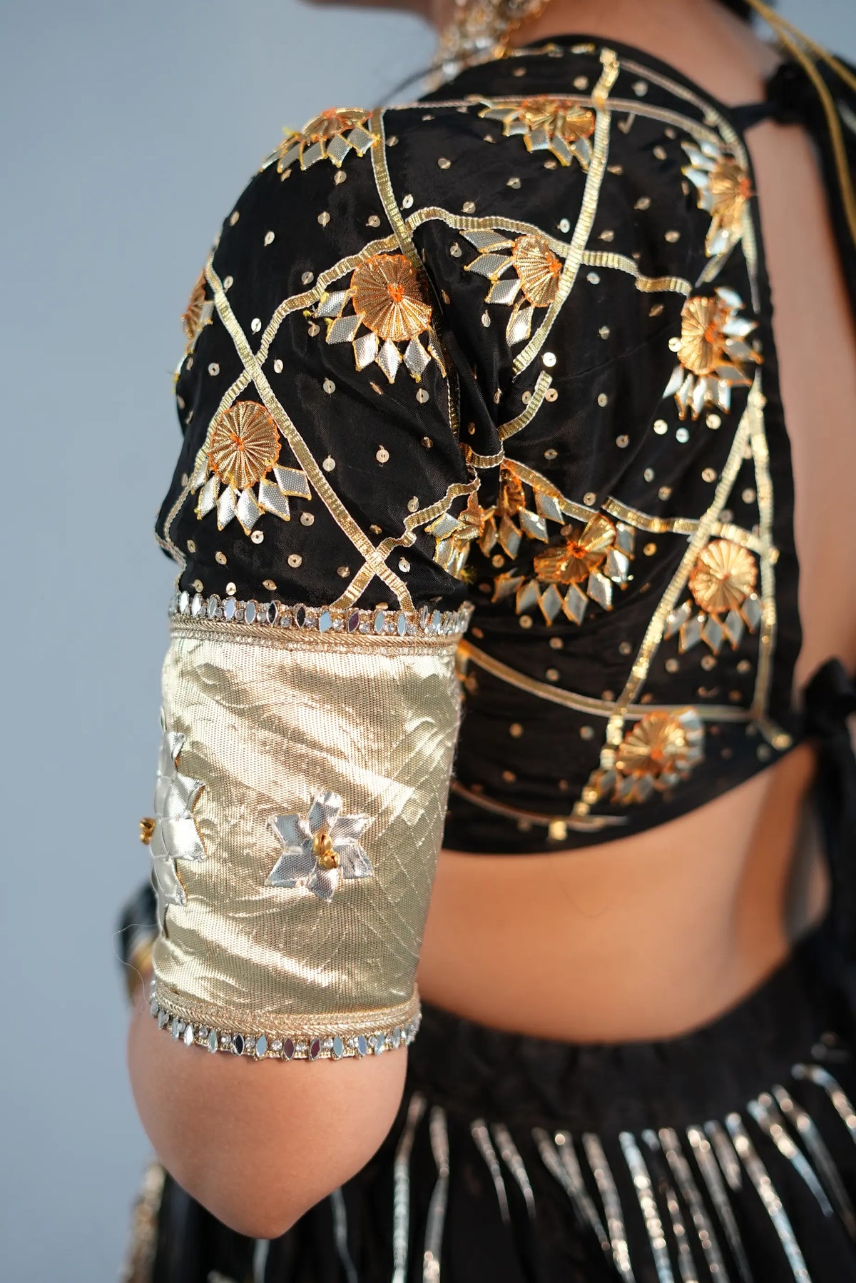 Close up of black custom aangi blouse sleeve with gold gota patti and flower motif embroidery