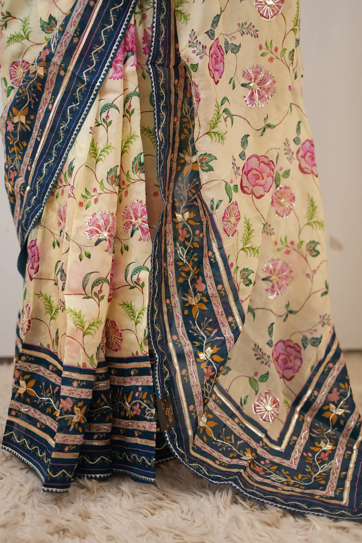 Front drape pose of model in cream tissue silk saree with peacock blue printed border