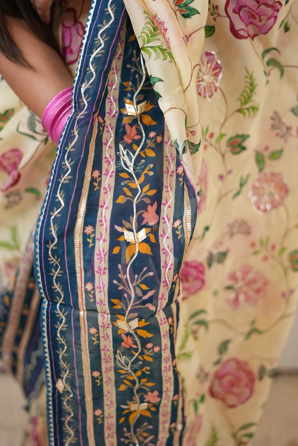 Close up view of peacock blue border showing intricate gold gota patti and zigzag lace detailing on cream tissue saree