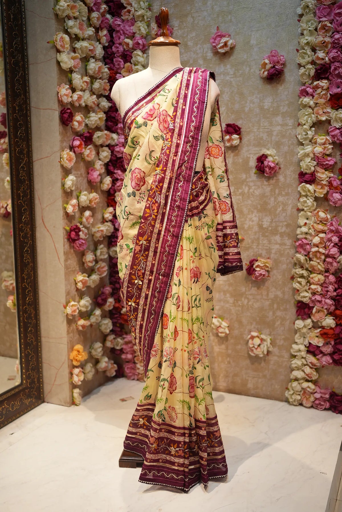Full mannequin display of cream printed tissue silk saree with rich maroon floral border and gota patti work