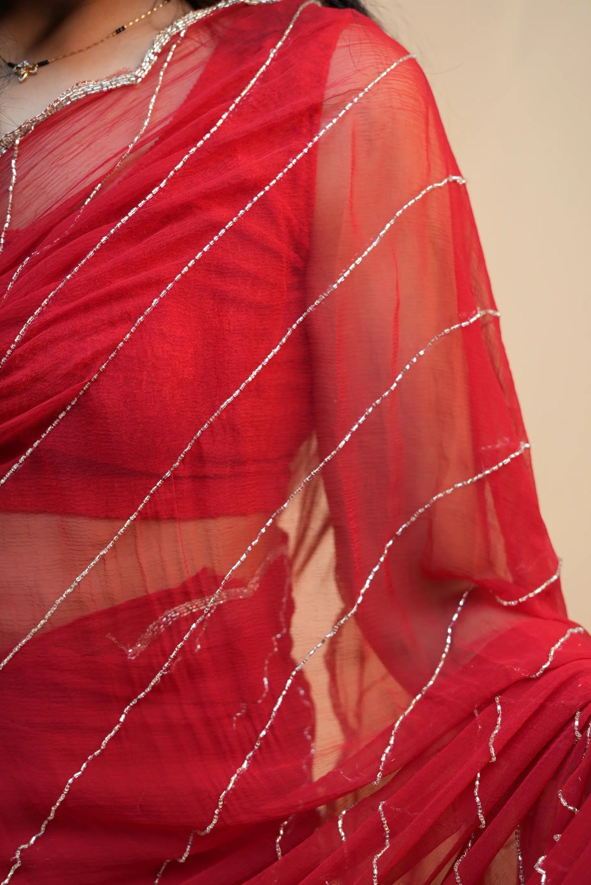 Close up view of crimson red pure chiffon saree showing diagonal cutdana and zari beaded lines
