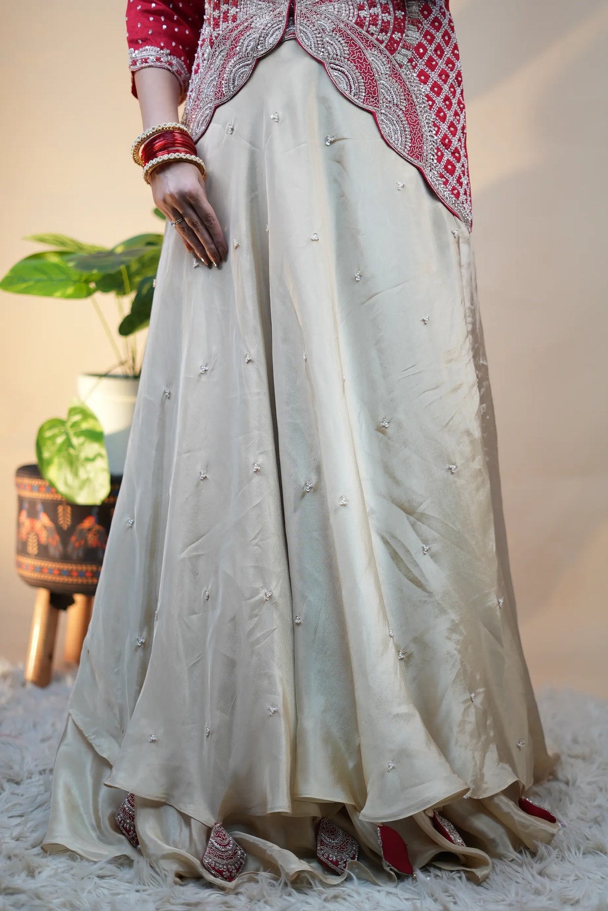 Mid shot of model displaying layered off-white skirt and fitted red jacket with rich embroidery