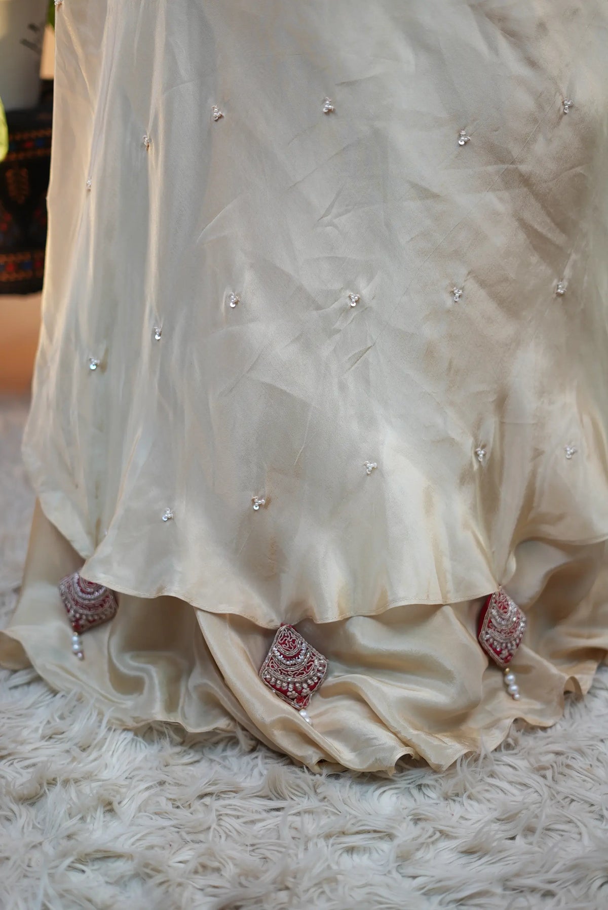 Close-up shot of off-white golden skirt hemline displaying red embroidered latkan drops with pearls