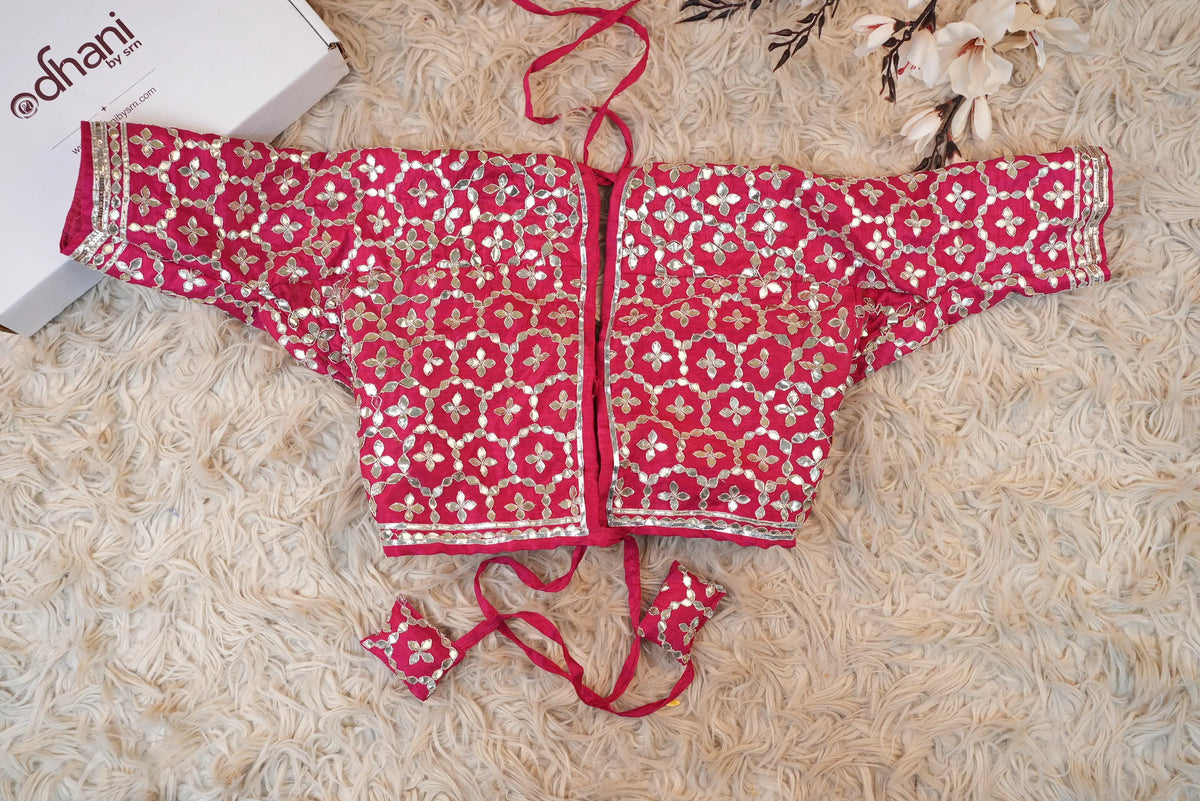 Flat lay layout of sample rani pink Rajasthani Aangi blouse showing open back design and matching embroidered latkans
