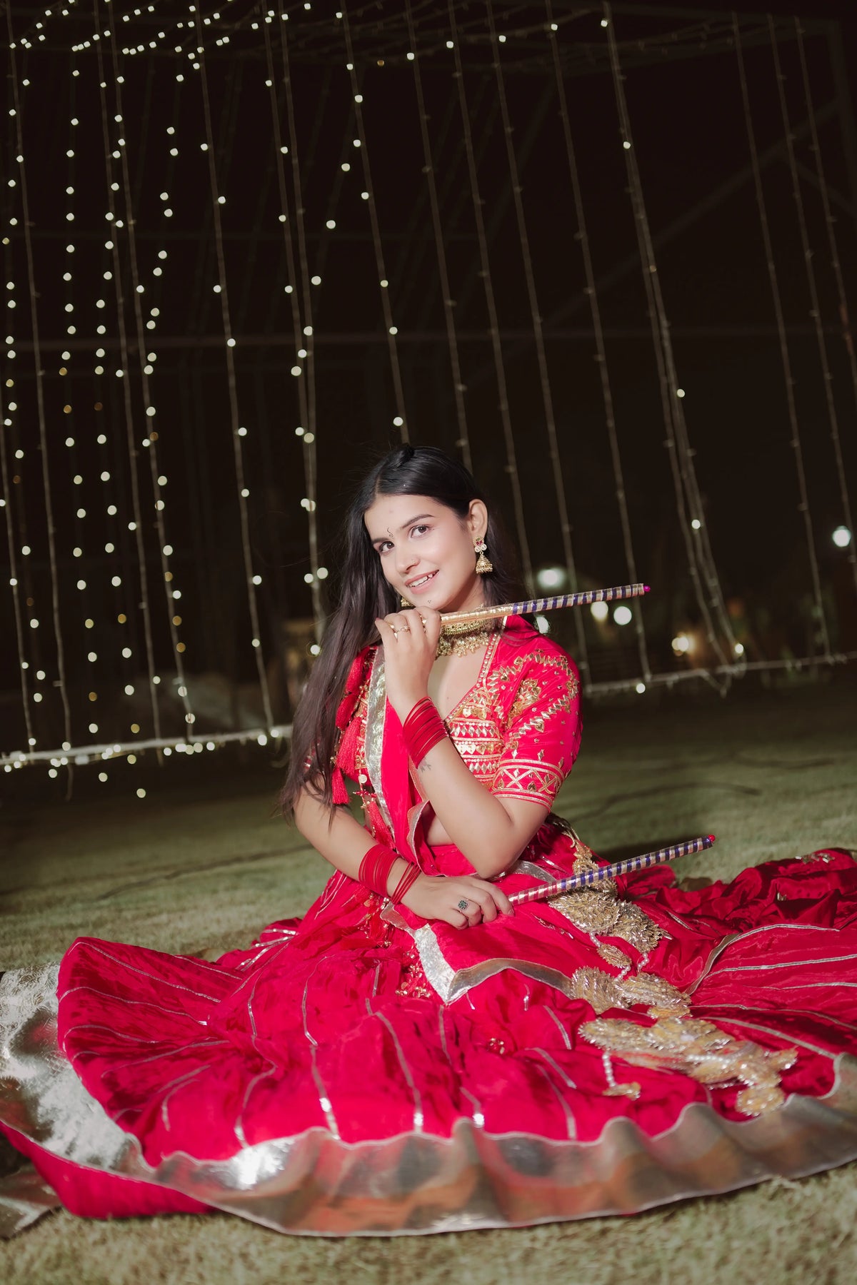 Seated pose of model showcasing full flare red crepe lehenga set with aangi blouse and ghungroo dupatta