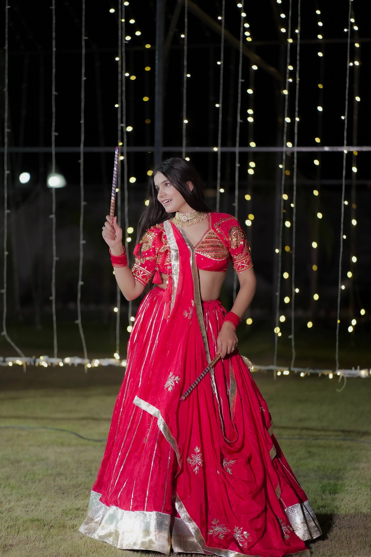 Model twirling in red pure crepe lappa lehenga with dandiya sticks for Navratri garba look