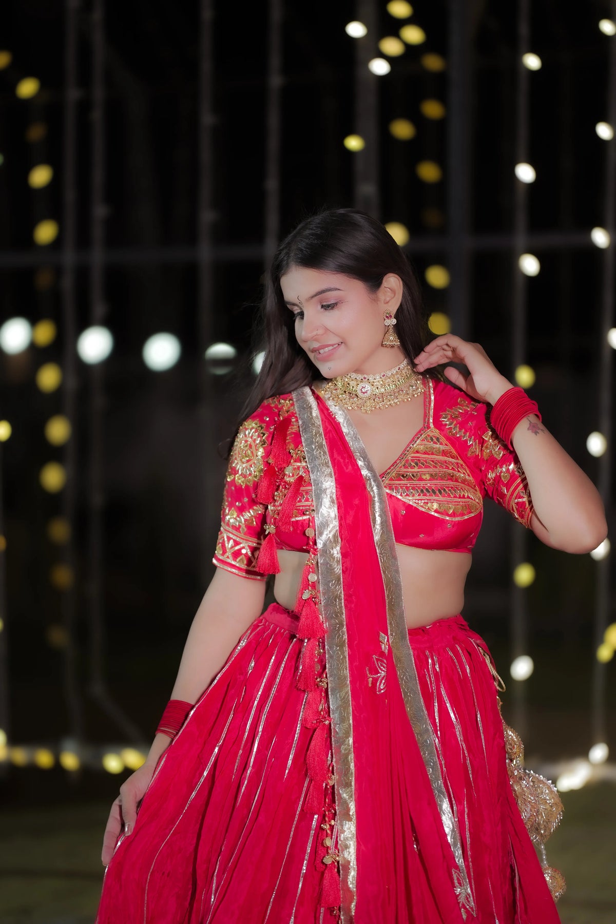 Front pose of model in red crepe lappa lehenga set holding dupatta with embellished tassel hangings
