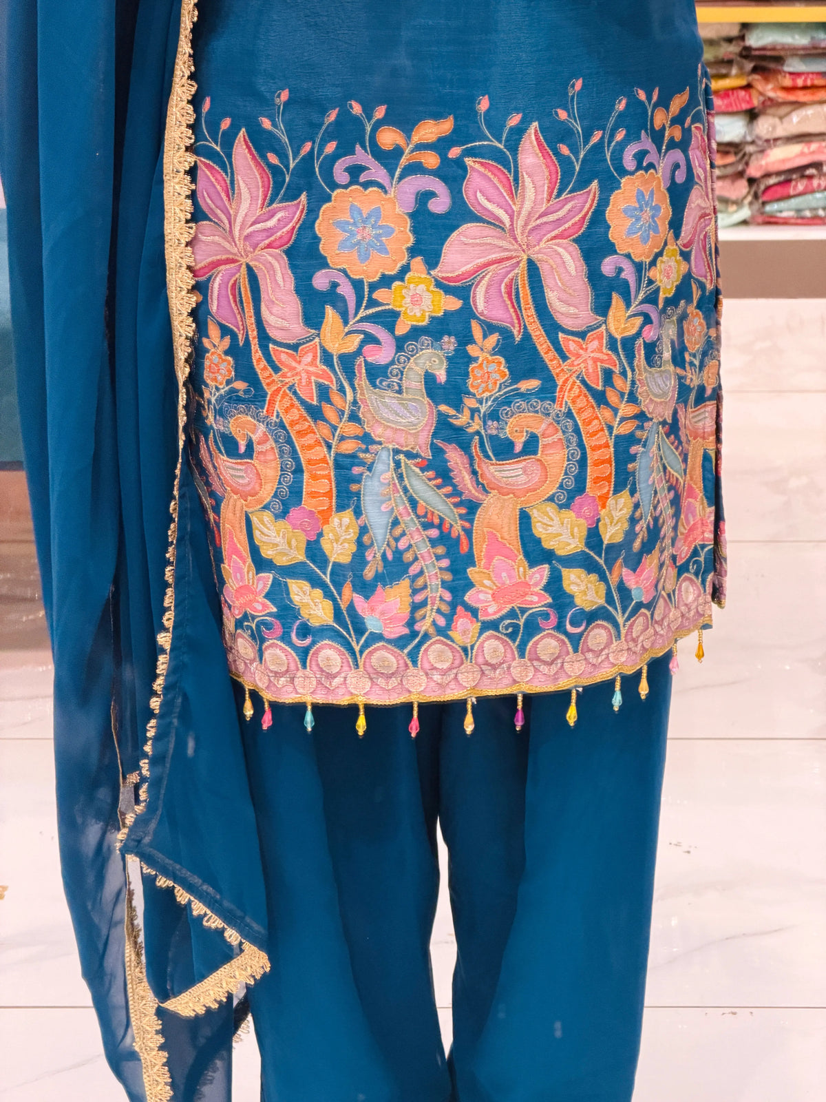 Close-up view of multi-color peacock brush painting, sequin embroidery, and bead tassels on Kurti daman