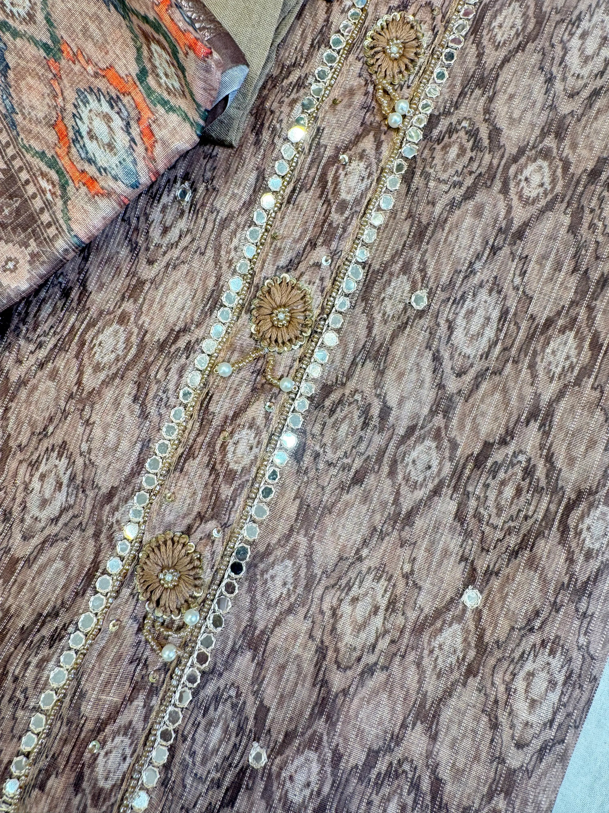 Macro photo of intricate mirror work, cutdana piping, and pearl moti handwork on tissue suit neckline