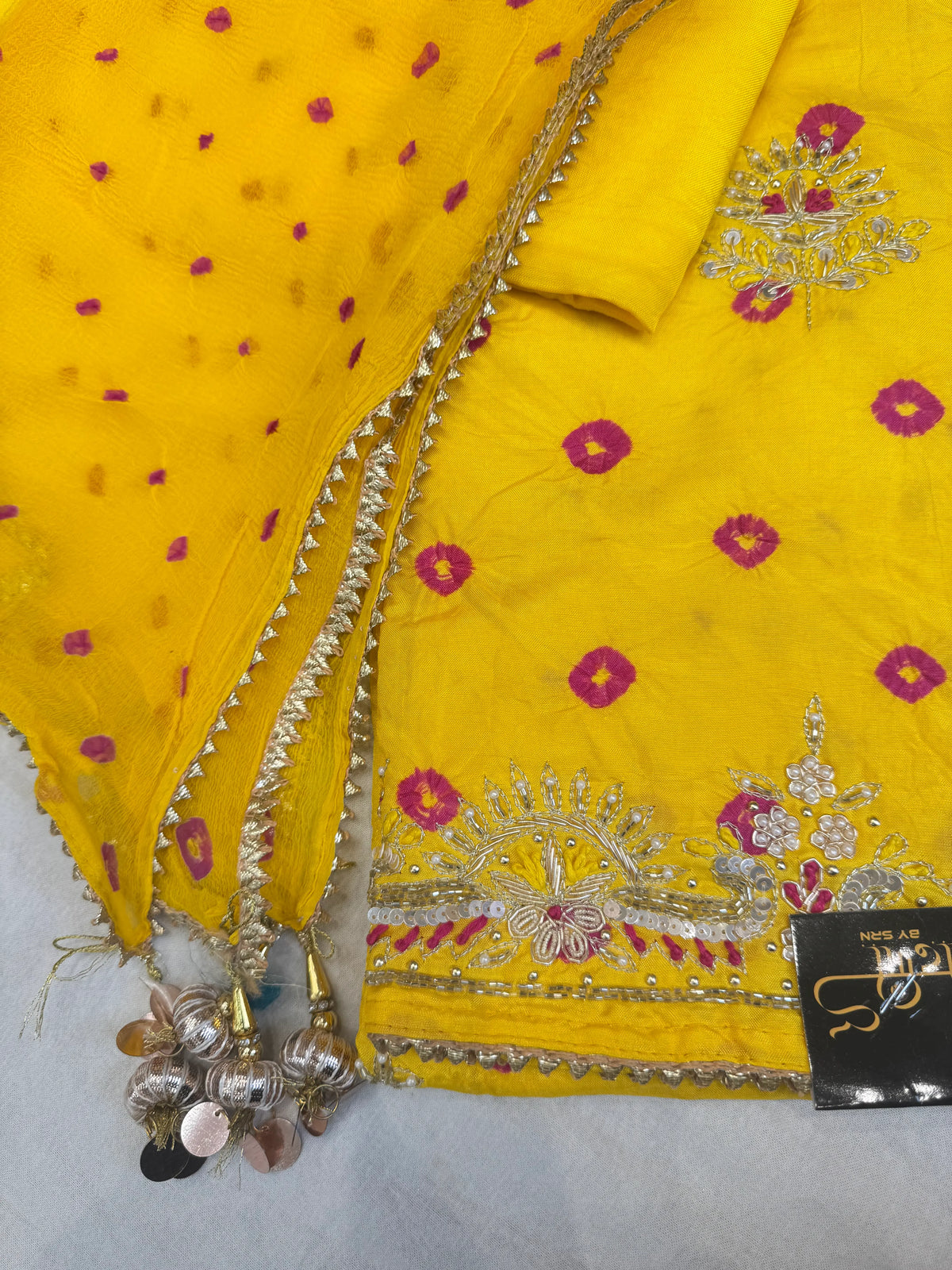 Flat lay view of yellow silk bandhej unstitched suit material featuring zardozi daman work and embellished dupatta with latkans