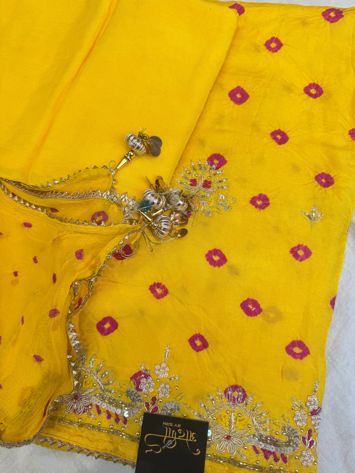 Top angle shot showing yellow bandhej dupatta lace border with decorative handcrafted tassels and suit piece