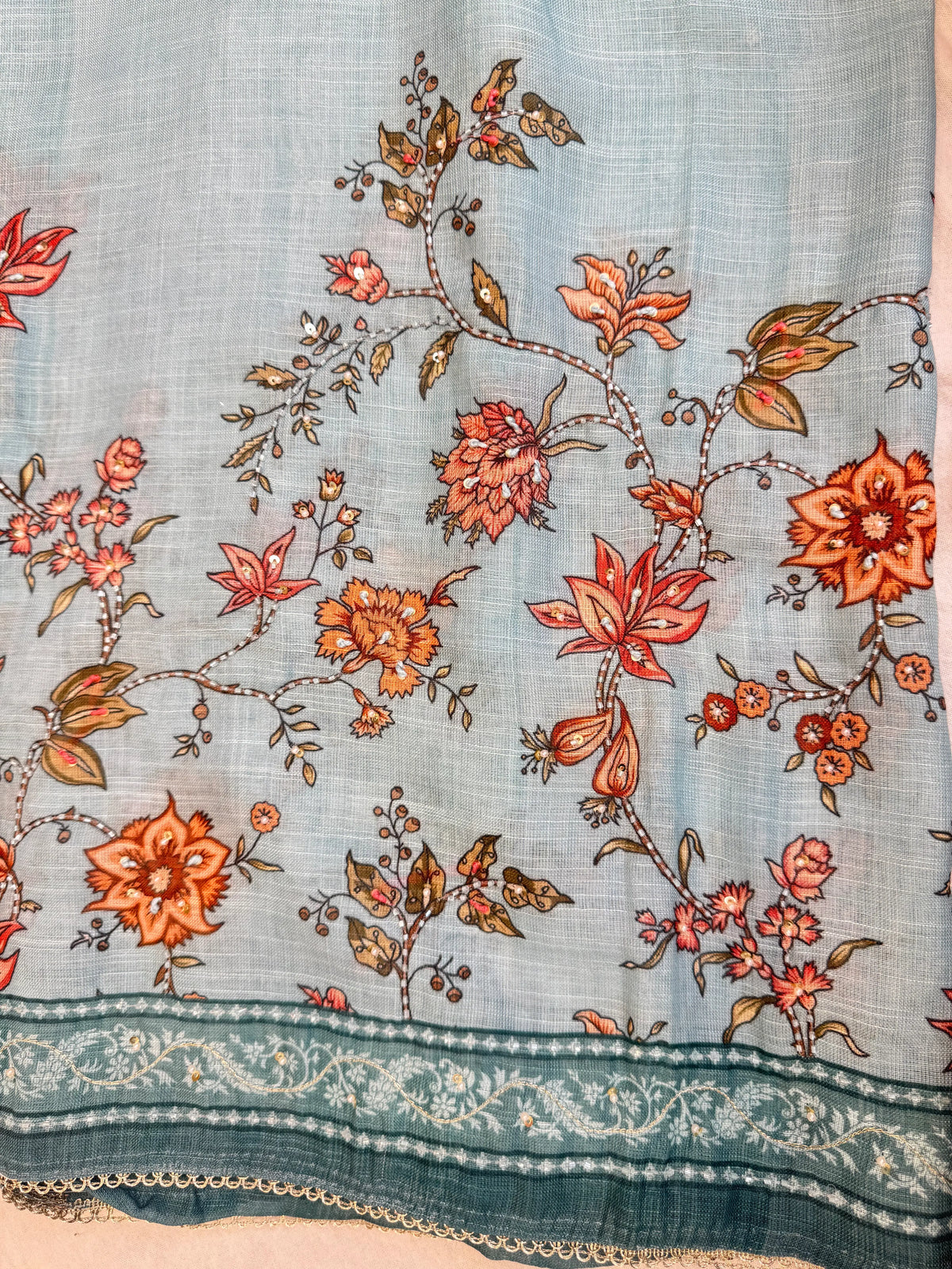 Close up view of sky blue cotton doria fabric featuring hand embroidered orange flowers with cutdana and white pearls