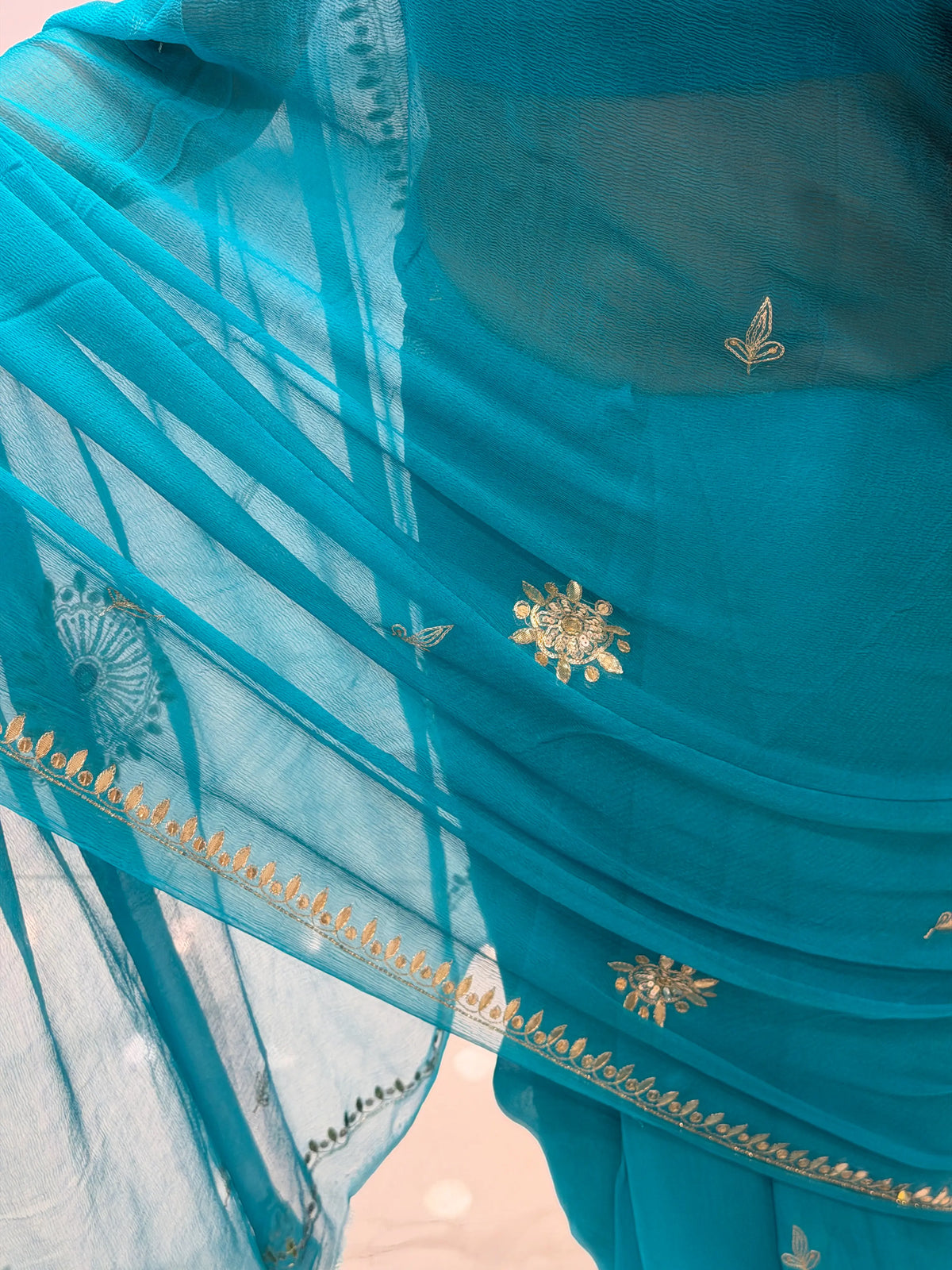 Close-up view of Peacock Blue Pure Chiffon fabric showing hand-embroidered leaf buttis and border