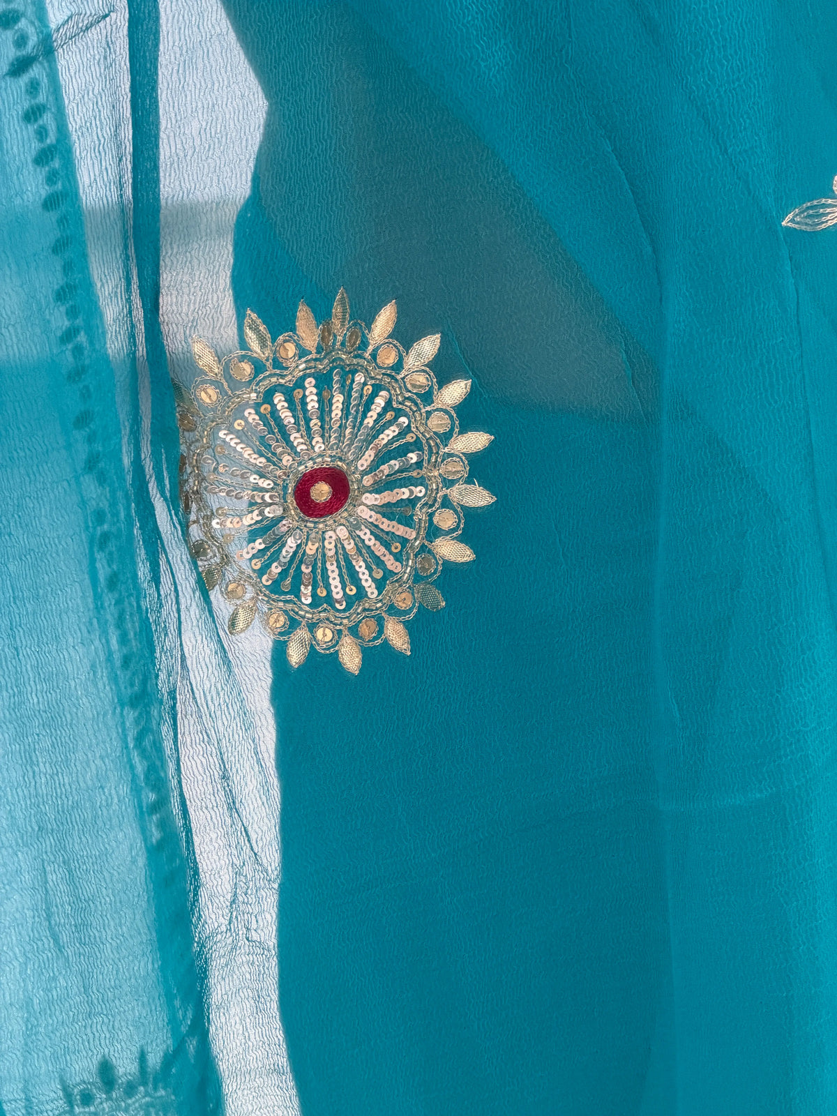Detailed macro shot of sun-inspired circular chakra motif with maroon thread center on blue chiffon